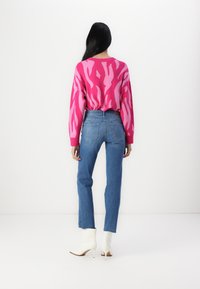 Suéter de punto fucsia con un patrón abstracto, combinado con jeans de cintura alta azules y botas de tobillo blancas. Fondo minimalista.