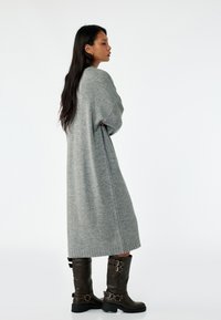 Over-sized, langafas grijze gebreide jurk met een losse pasvorm. Gepaard met kniehoge bruine leren laarzen met gespen. Vriendelijke textuur.