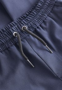 Vita elasticizzata blu navy con coulisse nera e occhielli in metallo su tessuto intrecciato, che mostra cuciture dettagliate e trama.