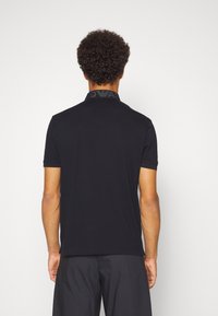 Svart pikétröja med en texturerad krage som har logodetalj. Korta ärmar, figurnära design, tillverkad i en mjuk bomullsblandning.