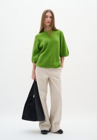 Green knit oversized sweater, beige wide-leg trousers, and a black fabric tote bag. The sweater features a textured pattern and relaxed fit.