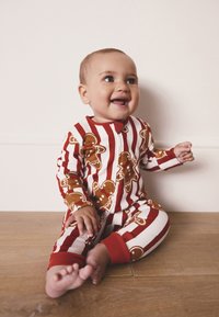 Czerwone piżamy w paski z wzorem piernikowych ludzików, z czerwonym kołnierzem i mankietami, wykonane z miękkiej tkaniny, odpowiednie dla niemowląt.