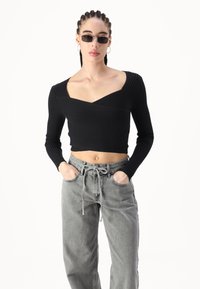 Top corto de manga larga negro con diseño de escote en V, combinado con jeans grises holgados que tienen una cintura con cordón y bolsillos frontales.