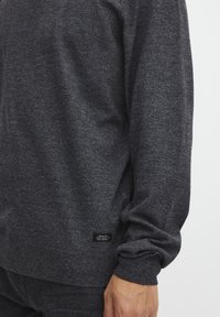 Pullover-Sweater in Anthrazitgrau aus strukturierter Stoff, mit gerippten Bündchen und Saum, und einem kleinen Etikett am unteren Rand.