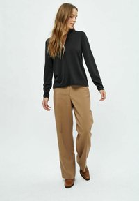 Sort langærmet top med v-hals, parret med højtaljede beige vidde bukser. Brune ankelstøvler fuldender outfittet.