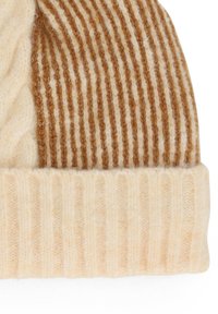Berretto lavorato a maglia in crema e beige, con un design testurizzato a costine caratterizzato da strisce alternate e un risvolto nella parte inferiore.