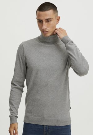 Grauer Rollkragenpullover aus weichem Strickstoff, mit langen Ärmeln und geripptem Kragen und Saum. Getragen mit Jeans.