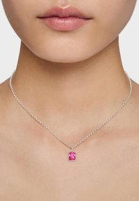Collana con catenina d'argento e piccolo pendente a forma di orsetto gommoso rosa sul collo e area della clavicola di una persona.