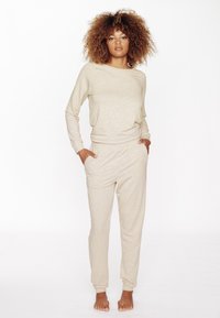 Ensemble de salon beige en tissu doux, comprenant un haut à manches longues avec un col rond et un pantalon de coupe décontractée avec poches.