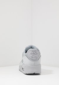 Pelēkie Nike Air sporta apavi ar mīkstinātu valni, sieta augšdaļu, teksturētu papēdi un redzamu gaisa amortizāciju zolē.
