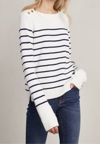 Vit och marinblå randig tröja med rundad hals, guldaccentknappar på axlarna och långa ärmar. Matchad med blåjeans.