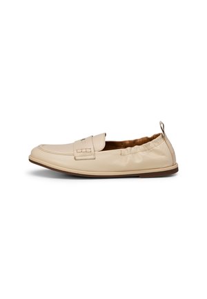 Beige leren instaploafer met elastische achterkant, gestikte bovenkant en platte bruine zool, zijaanzicht op witte achtergrond.
