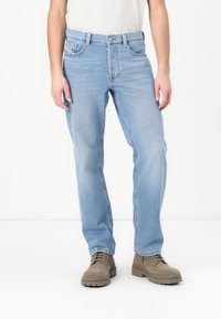Light blue denim jeans with a classic cut, featuring front pockets and belt loops, paired with brown suede boots. Smooth fabric texture.