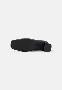 Escarpin noir à talon aigu avec une tige lisse et une semelle en caoutchouc texturée. Le design présente un bout carré et un talon épais modeste.