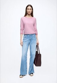 Lichtroze gestreepte top met lange mouwen gecombineerd met lichtblauwe wijde spijkerbroek, een donkerbruine shopper vasthoudend, en zwarte en witte sneakers dragend.