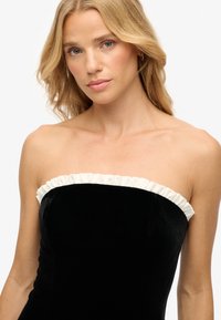 Zwart strapless fluwelen jurk met een witte gerimpelde halslijn. Soepele textuur en aansluitend ontwerp, met een slanke silhouet.