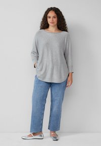 Lichtgrijze lange mouw top met een ronde hals, gecombineerd met lichtblauwe recht-toe-rechtdoor spijkerbroek en zilveren ballerina's. De top heeft een ontspannen pasvorm.