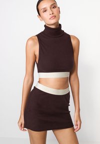 Hnědý žebrovaný crop top s vysokým límcem a odpov�ídající mini sukní. Obsahuje světle šedý elastický pásek s reliéfním nápisem.