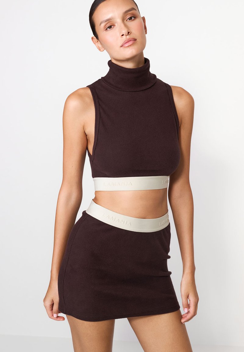 Hnědý žebrovaný crop top s vysokým límcem a odpovídající mini sukní. Obsahuje světle šedý elastický pásek s reliéfním nápisem.