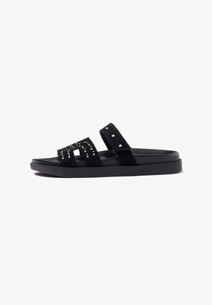 Schwarze Wildledersandalen mit zwei breiten Riemen, verziert mit quadratischen Metallnieten. Sie haben eine strukturierte, gepolsterte Sohle und ein flaches Design.