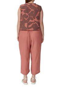 Haut sans manches, ample, dans un motif abstrait brun et rouille, associé à un pantalon court léger rose et des sandales à lanières.