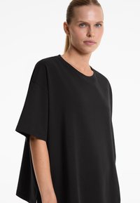 Fekete, túlságosan nagy póló, puha pamutból készült, kerek nyakkivágással és rövid ujjakkal, laza fazonú és minimalista dizájnnal.