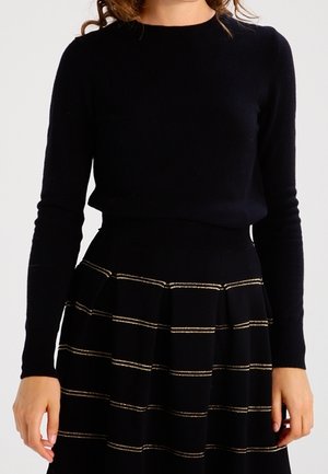 Pull noir en tricot à manches longues associé à une jupe noire avec des rayures horizontales dorées, un tissu texturé et un design plissé.
