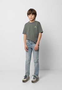 Camiseta de algodón gris con un pequeño gráfico de calavera neón, combinada con jeans ajustados azul claro y zapatillas grises con acentos verdes.