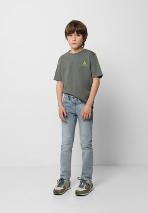 Camiseta de algodón gris con un pequeño gráfico de calavera neón, combinada con jeans ajustados azul claro y zapatillas grises con acentos verdes.