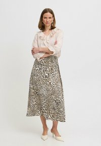 Light beige blouse with ruffled neckline, paired with a leopard print midi skirt in tan and black. White heeled mules complete the look.