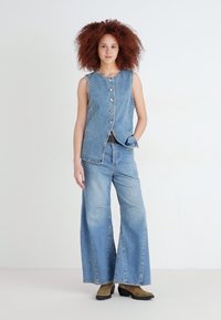 Jeansväst med silverknappar och vida jeans i ljusblå tvätt, som har en lös passform och minimal slitning. Mörka skor med tjock sula.