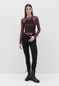 Top de rejilla negra de manga larga con patrones abstractos rojos y texto, combinado con jeans negros ajustados de cintura alta y botas de combate negras.
