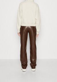 Sudadera de cuello alto color crema con hombros caídos combinada con pantalones anchos de cuero marrón. Textura suave con costuras entalladas y zapatillas deportivas en tonos neutros.