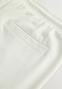 Gros plan sur un pantalon en tissu blanc avec une poche passepoilée cousue et une ceinture élastique en haut.