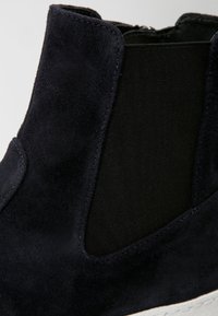 Bottine Chelsea en daim bleu marine avec des panneaux latéraux en élasthanne et une semelle texturée. Présente des coutures lisses et une silhouette élégante.