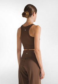 Brun sportig crop top med hög krage och racerback-design, i kombination med matchande byxor med hög midja. Slät textur, minimal varumärkesprofil.