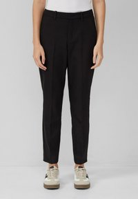 Zwarte op maat gemaakte broek met een platte voorkant, taps toelopende pijpen en riemlussen, gecombineerd met beige en zwarte sneakers voor een casual look.