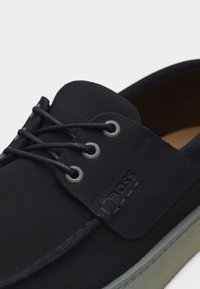 Μαύρο δερμάτινο παπούτσι τύπου boat με στρογγυλά κορδόνια, μεταλλικά οπές και ανάγλυφο λογότυπο BOSS στο πλάι, με ανοιχτόχρωμη σόλα.