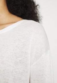 Maglione bianco a maglia con una texture morbida e sottile. Ha una vestibilità rilassata, un ampio scollo e spalle basse.