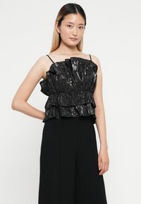 Fekete, fényes pántos top réteges fodrokkal és vékony pántokkal. Különlegesen anyagú, gyűrött mintázatú, és fitted sziluettjével rendelkezik.