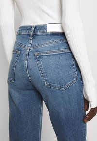 Blauwe spijkerbroek met hoge taille, ontwerp met vijf zakken, contrasterende stiksels en een wit label op de achterste tailleband.