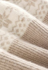 Maglione lavorato a maglia di un tan chiaro con un motivo crema, texture morbida, dettagli a coste e sottili filamenti metallici.