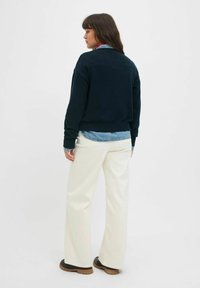 Tumši zils pārspīlēts džemperis ar gaismas zilas džinsa krekliem, apvienots ar plaša piegriezuma krēmkrāsas biksēm un melnām zābakiem. Gludas tekstūras, ikdienas piegriezums.