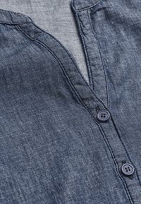 Jeansshirt med krage, lavet af mørkeblåt materiale, med to knapper foran og en blød, tekstureret overflade.