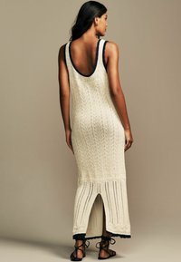 Abito maxi in maglia crema con scollo a V profondo e finiture blu navy. Presenta un motivo a foglia, spacco laterale e dettagli a coste sull'orlo.