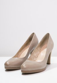 Chaussures beiges à talons hauts avec une tige en cuir lisse, un bout arrondi et une semelle intérieure à motif texturé. Le talon empilé épais ajoute de la stabilité.