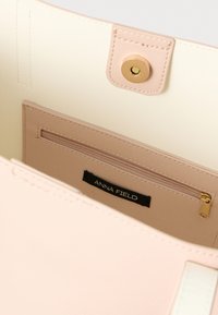 Innenansicht einer beigen Handtasche mit einem Reißverschlussfach mit goldenem Reißverschluss und einem schwarzen Etikett mit der Aufschrift Anna Field.