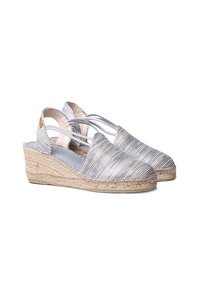 Espadrillas a zeppa in tessuto argentato intrecciato con suole in juta intrecciata, aperte sul retro e con cinturini elastici per una vestibilità sicura. Superficie testurizzata con un interno liscio.