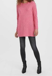 Vaaleanpunainen pitkähihainen neulepaita, jossa on pyöreä pääntie ja ribbireunat. Asusteena slim fit -mustat farkut ja teräväkärkiset nilkkurit.