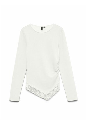 Chemise blanche manches longues avec col rond, ourlet asymétrique avec bordure en dentelle et détails froncés sur le côté.